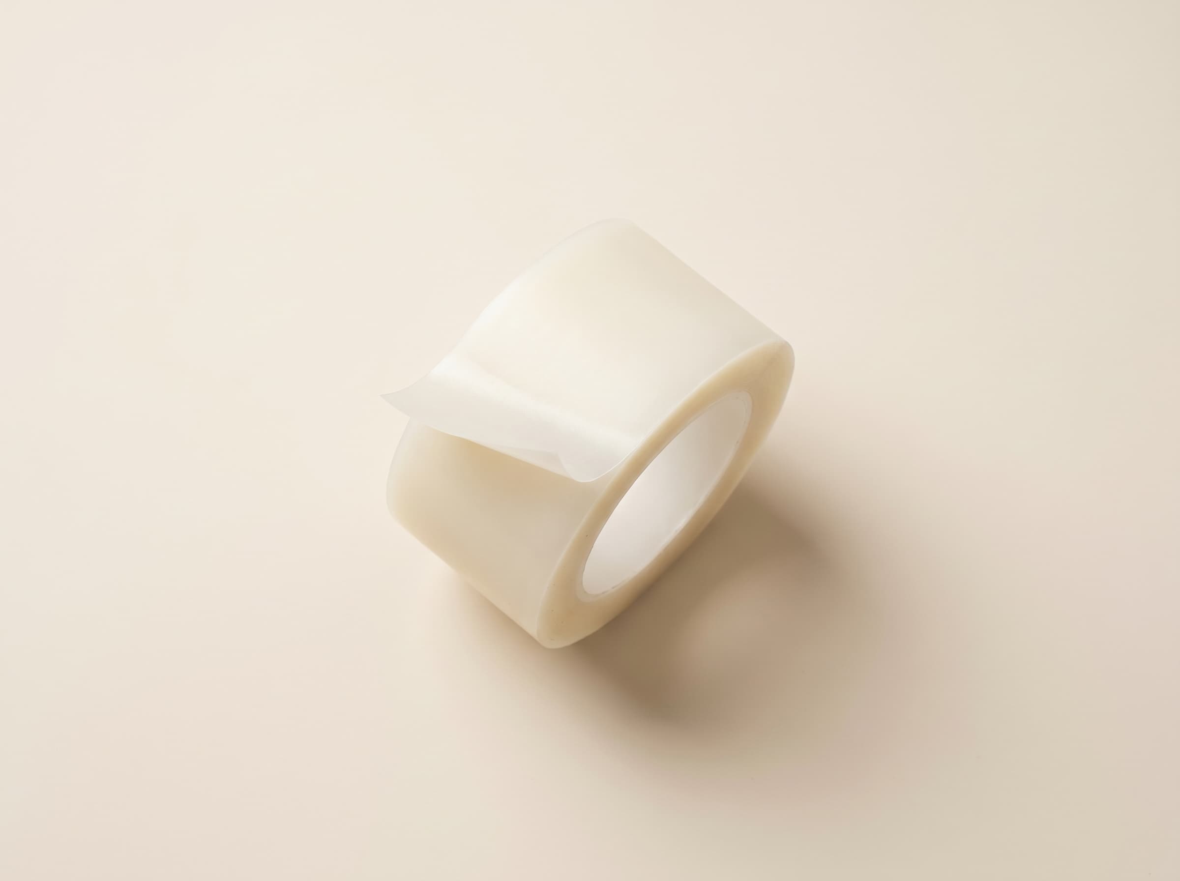 Roll of translucent MEND hydrocolloid tape with the end peeled back, on a cream background